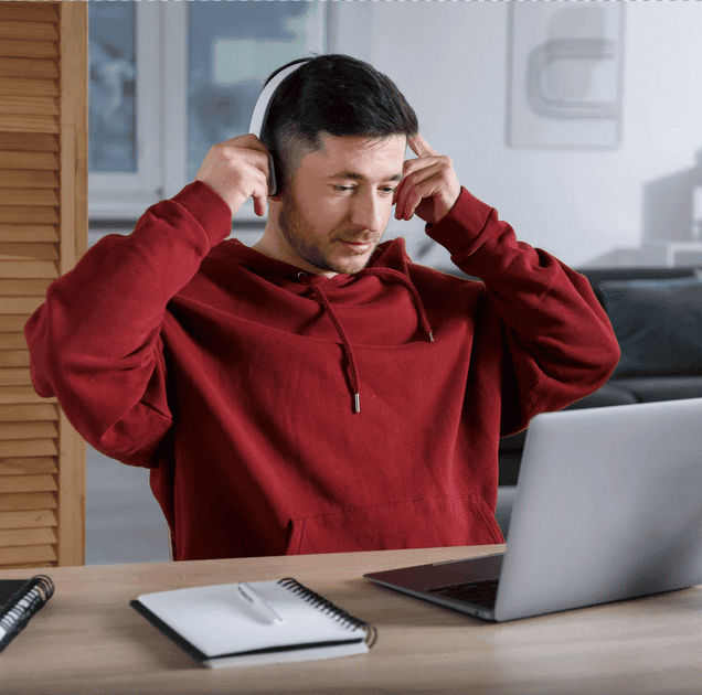 man seated at laptop putting on headphones